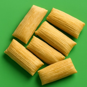 Half dozen tamales with corn husks on a green background in Dallas.