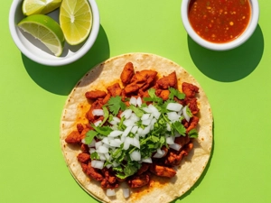 Al Pastor Taco with diced onion and cilantro, served with lime wedges and salsa in Dallas.