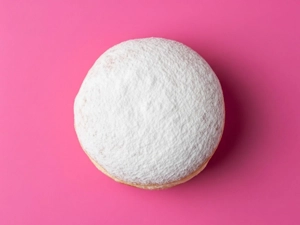 Apple Jelly Donut with powdered sugar on a pink background in Dallas.