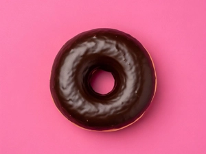Chocolate glazed donut with a shiny chocolate coating on a pink background in Dallas.