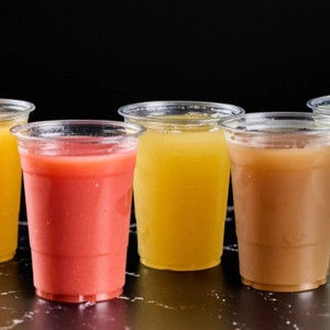 Vasos de plástico con jugos de colores rojo, amarillo y marrón. Cocina desconocida en ciudad desconocida.