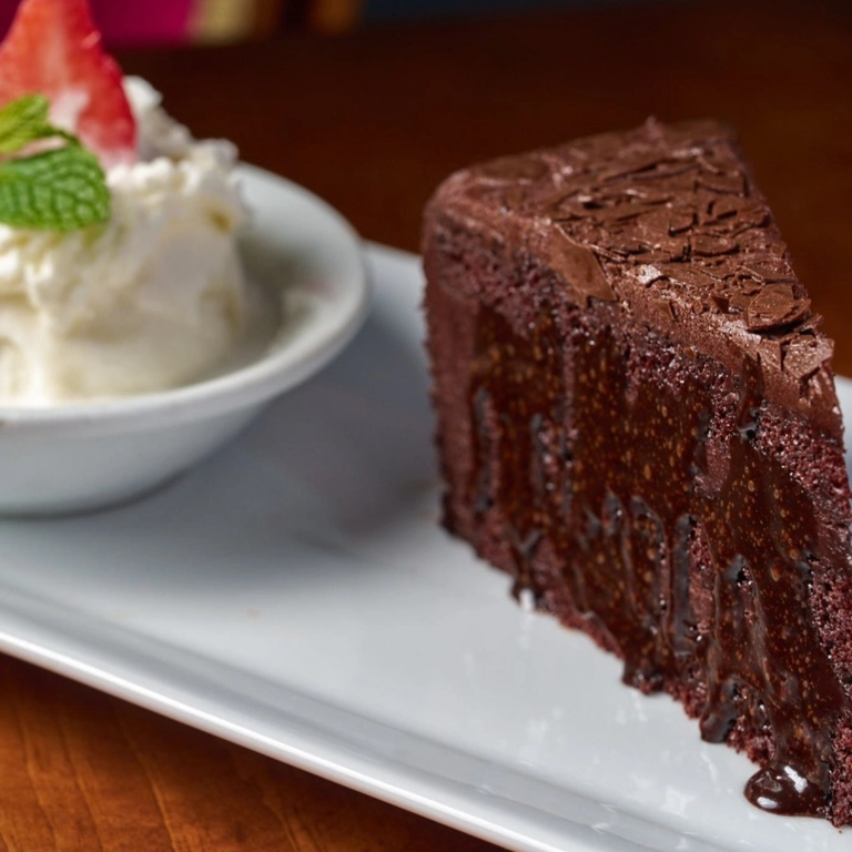 Chocolate cake slice with chocolate frosting and a side of whipped cream topped with a strawberry in Wantagh.