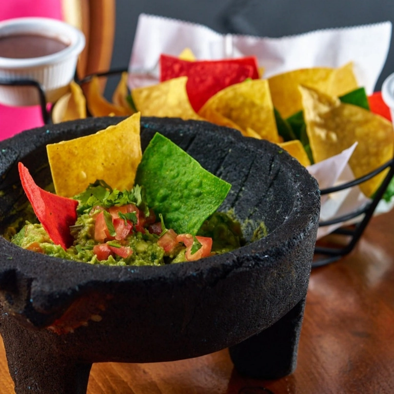 Guacamole Molcajete with chopped tomatoes and cilantro, served with colorful tortilla chips in Wantagh.