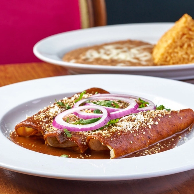 Enchiladas de Mole Poblano with red mole sauce, topped with sliced red onions and cheese in Wantagh.