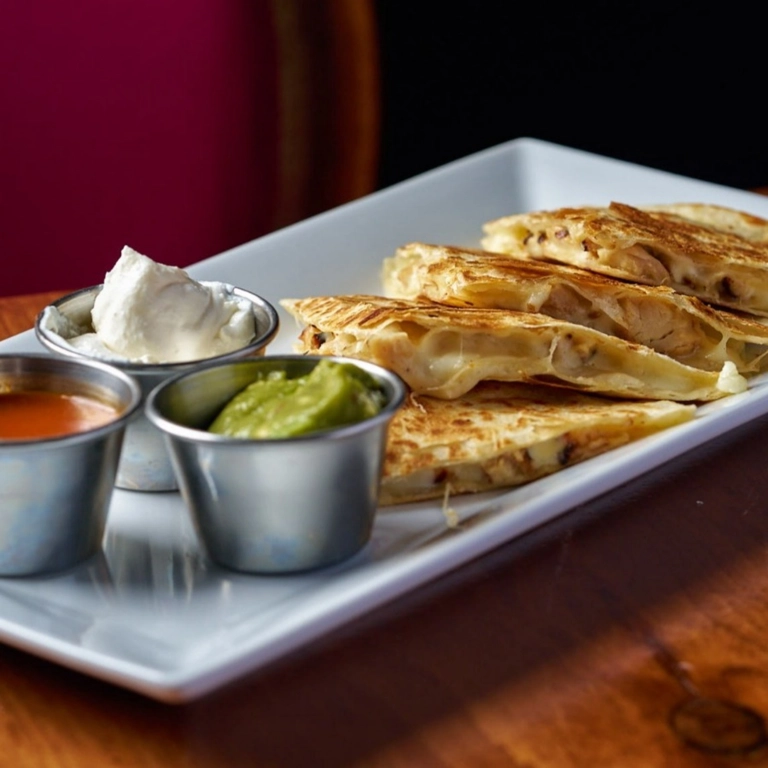 Gringa Quesadilla Steak with melted cheese and steak slices, served with sour cream, guacamole, and salsa on a white plate