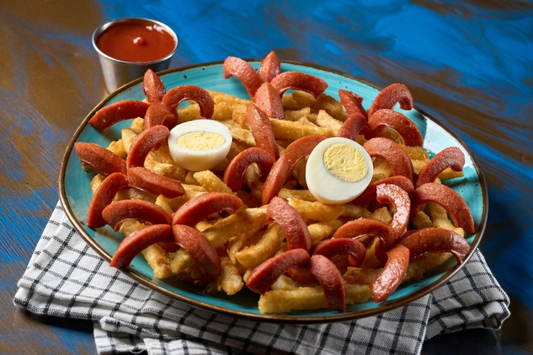 Salchipapas con papas fritas, salchichas y huevo cocido. Salsa roja al lado. Ciudad desconocida.