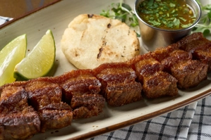 Chicharrón con arepa, acompañado de rodajas de limón y salsa verde, en un plato.