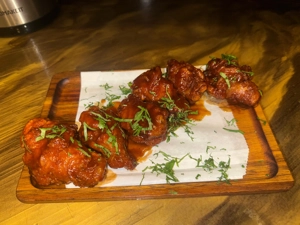 Alitas de pollo con salsa roja y cilantro picado, servidas en una tabla de madera. Ciudad desconocida.