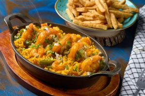 Arroz con camarones con cebollín y arroz amarillo en sartén, acompañado de papas fritas. Cocina desconocida en ciudad
