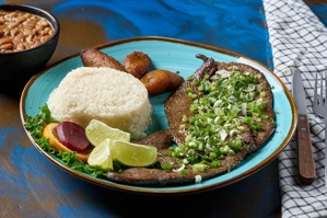 Hígado encebollado con cebolla y arroz blanco, acompañado de frijoles y plátanos maduros. Cocina desconocida en ciudad