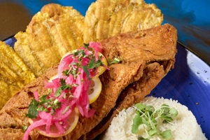 Pargo rojo frito con arroz blanco y tostones visibles en el plato, en una ciudad desconocida.