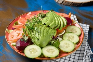 Ensalada de aguacate con rodajas de pepino y tomate, visible en un plato en una mesa. Cocina desconocida en ciudad