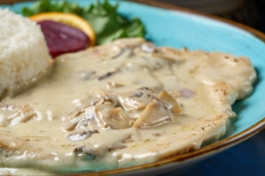 Pechuga en salsa de champiñones con arroz blanco y ensalada. Champiñones y salsa visibles en el plato. Ciudad desconocida.