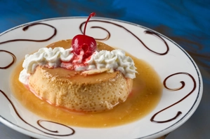 Flan con crema batida y cereza en un plato decorado, cocina desconocida en ciudad desconocida.