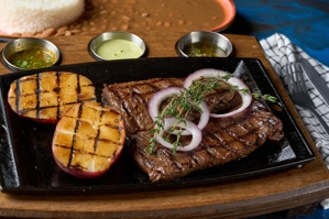 Entraña a la parrilla con aros de cebolla y rodajas de papa asada, acompañada de arroz y frijoles. Tipo de cocina