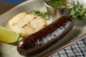 Morcilla con arepa acompañada de una rodaja de limón y salsa en un recipiente metálico. Cocina colombiana.