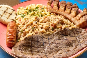 Desayuno Sabor a Colombia con huevos revueltos, arroz con frijoles, carne asada, chicharrón, salchicha y arepa en plato rojo.