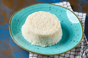Arroz blanco servido en un plato turquesa sobre un mantel a cuadros. Cocina desconocida en ciudad no especificada.