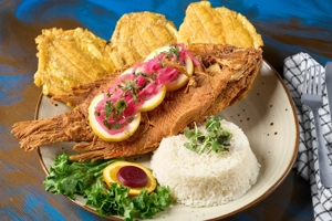 Mojarra frita con arroz blanco, tostones y ensalada. Plato de pescado frito con rodajas de limón y cebolla en la parte