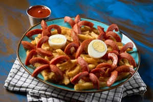 Salchipapas con papas fritas y salchichas, acompañadas de huevo cocido en un plato azul.