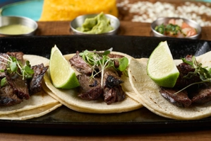 Tacos de arrachera con rodajas de limón y microvegetales sobre tortillas de maíz. Cocina mexicana, ciudad desconocida.