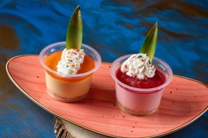 Mousse de mora con crema batida y una hoja decorativa. Dos porciones servidas en vasos transparentes sobre un plato ovalado.