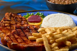 Chuleta con hueso a la parrilla con papas fritas, arroz blanco y ensalada. Cocina desconocida en ciudad desconocida.