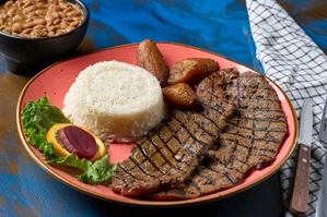 Carne asada con arroz blanco, frijoles y maduros. Incluye ensalada con lechuga y remolacha. Cocina desconocida en ciudad