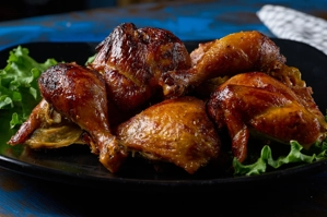 Pollo a la brasa peruano con piel dorada y lechuga en un plato negro.