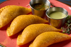 Empanadas colombianas de carne y pollo en un plato rojo, acompañadas de dos salsas en recipientes metálicos.