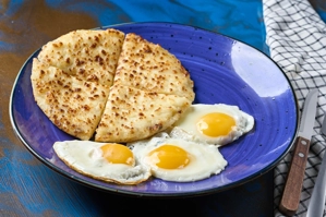 Huevos en cacerola con arepa, mostrando dos huevos fritos y una arepa en un plato azul. Cocina desconocida en ciudad no