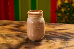 Milo en un tarro de vidrio con borde de chocolate en polvo sobre una mesa de madera. Sin identificar la ciudad.