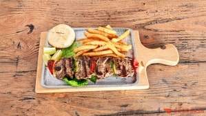 Chuzo de carne con arepa, papas fritas y rodajas de pimentón en una tabla de madera. Ciudad desconocida.
