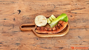 Chicharrón con arepa, rodajas de limón y lechuga en una tabla de madera. Cocina colombiana en una ciudad desconocida.
