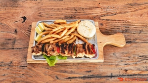 Chuzo de cerdo con papas fritas y arepa en una tabla de madera. Cocina desconocida, ciudad desconocida.