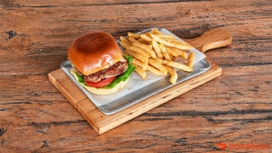 Hamburguesa de pollo con lechuga y tomate, acompañada de papas fritas en bandeja de metal.