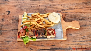 Chuzo Mixto con camarón y carne servidos con papas fritas y arepa en una tabla de madera.