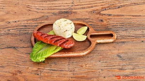 Chorizo con arepa servido sobre una hoja de lechuga con rodajas de limón en un plato de madera. Cocina desconocida.