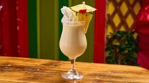 Piña Colada Virgen con crema batida y rodaja de piña en vaso decorado, fondo colorido.