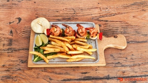 Chuzo de camarón con arepa, papas fritas y rodajas de limón en un plato sobre una mesa de madera.