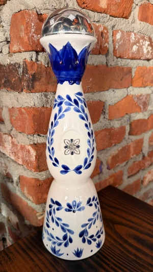 Botella de Clase Azul con diseño azul y blanco sobre una mesa de madera y fondo de ladrillo. No se puede determinar la