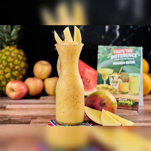Frozen De Mango Biche with mango slices and ice in a tall glass. Pineapple and apples in the background. Cuisine type and