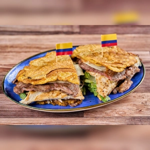 Toston Loco Mixto with plantains, beef, and cheese on a blue plate, featuring Colombian flags.