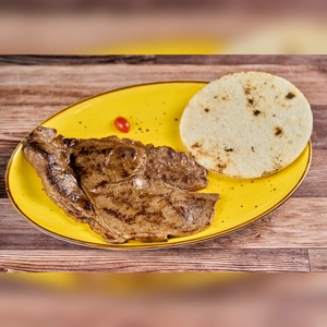 Carne Asada with Arepa on a yellow plate, featuring grilled beef and a round arepa. Unknown cuisine type and city.