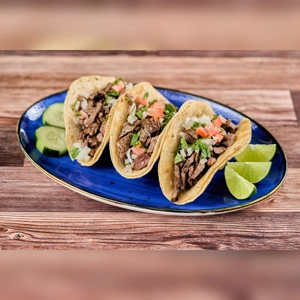 Mexican beef taquitos with diced onions, tomatoes, and cilantro on a blue plate. Served with lime wedges and cucumber
