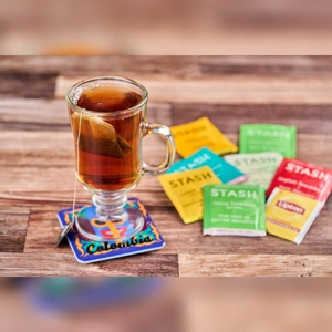 Glass of tea with a tea bag on a colorful coaster labeled 'Colombia', surrounded by various tea packets.