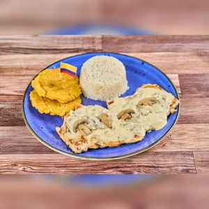 Pechuga en Salsa de Champiñones with mushroom sauce, tostones, and rice on a blue plate. Colombian cuisine.