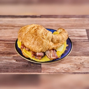 Croissant with egg and bacon, featuring a flaky pastry, scrambled eggs, and crispy bacon slices. Cuisine type and city