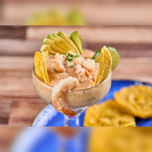 Shrimp ceviche with avocado slices and plantain chips, served alongside tostones in an unknown city.