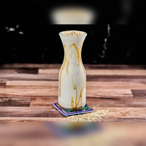 Avena Casera Fria with visible oats and caramel drizzle in a glass jar. Cuisine type and city unknown.